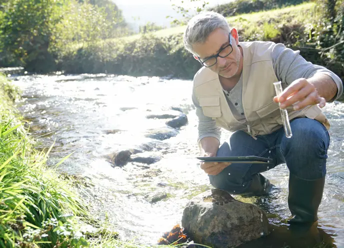 A man holding a tablet in a stream testing the water.